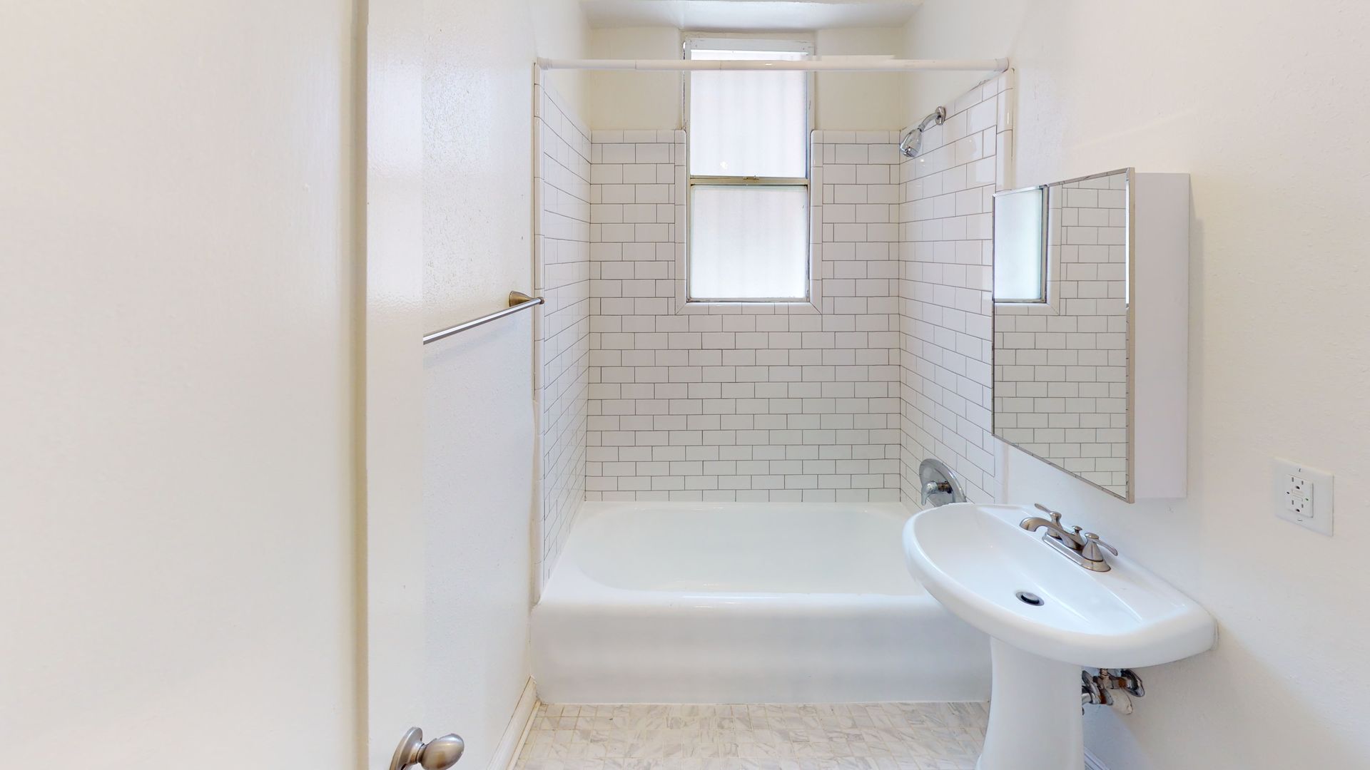 Small, white bathroom with a shower, sink, and mirror. White brick tile in the shower area.