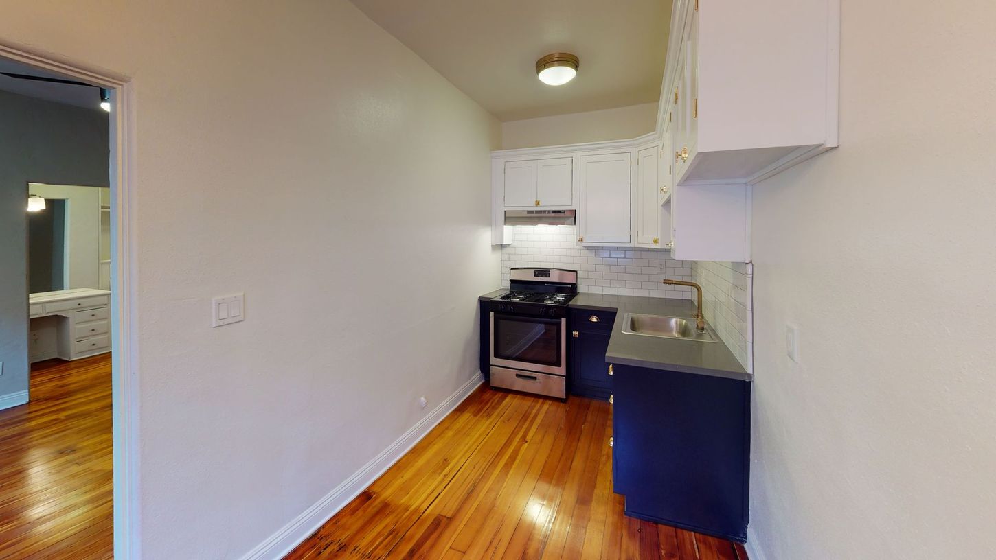 Narrow kitchen with blue and white cabinets, stove, and hardwood floors.