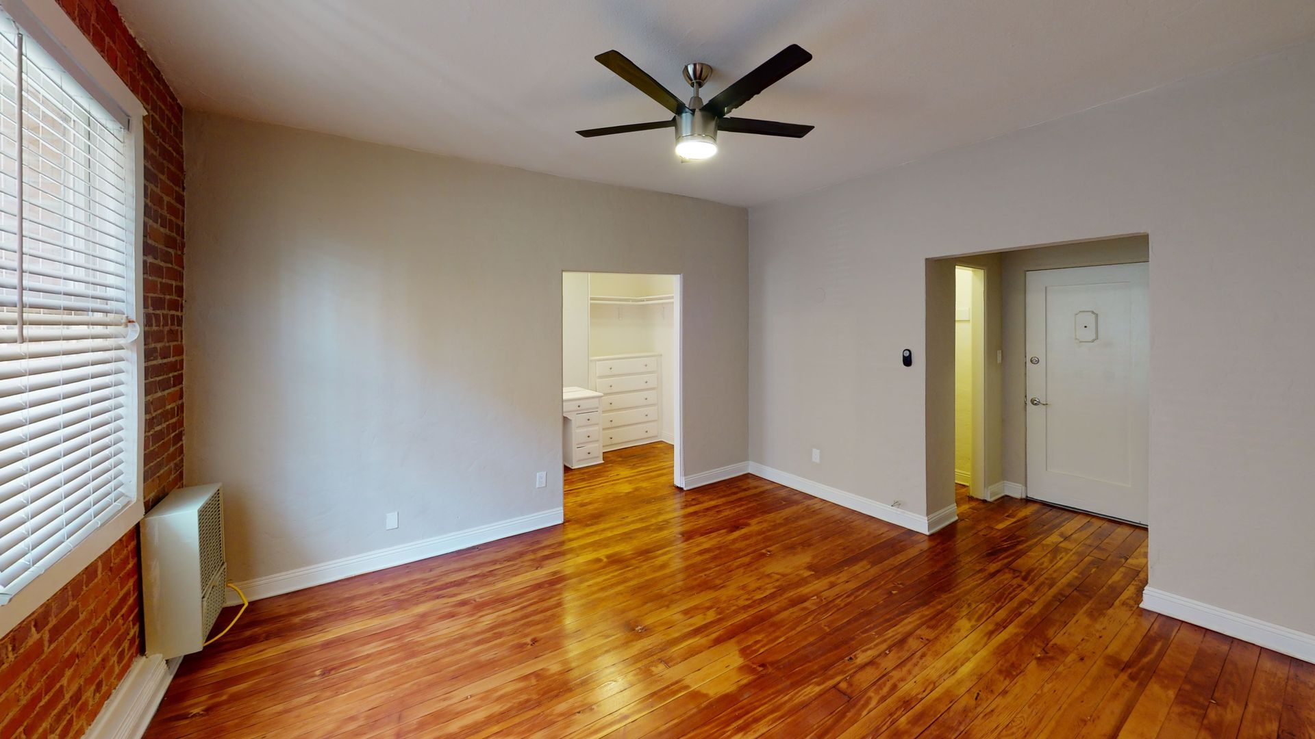 Interior view of a room with hardwood floors, exposed brick wall, and entryways to other rooms.