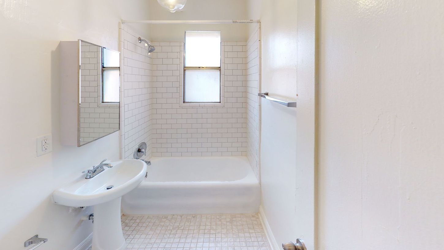White bathroom with a tub, sink, mirror, and window.