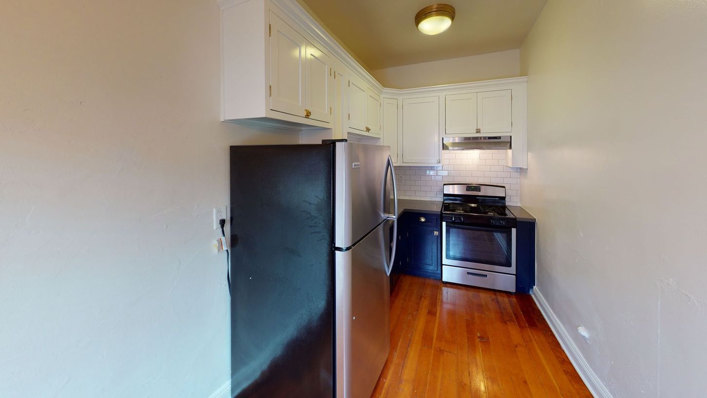 Small kitchen with white cabinets, stainless steel refrigerator and stove, wood floor.