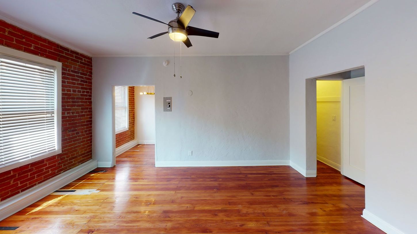 Empty living room with exposed brick wall, hardwood floors, and doorway to another room.