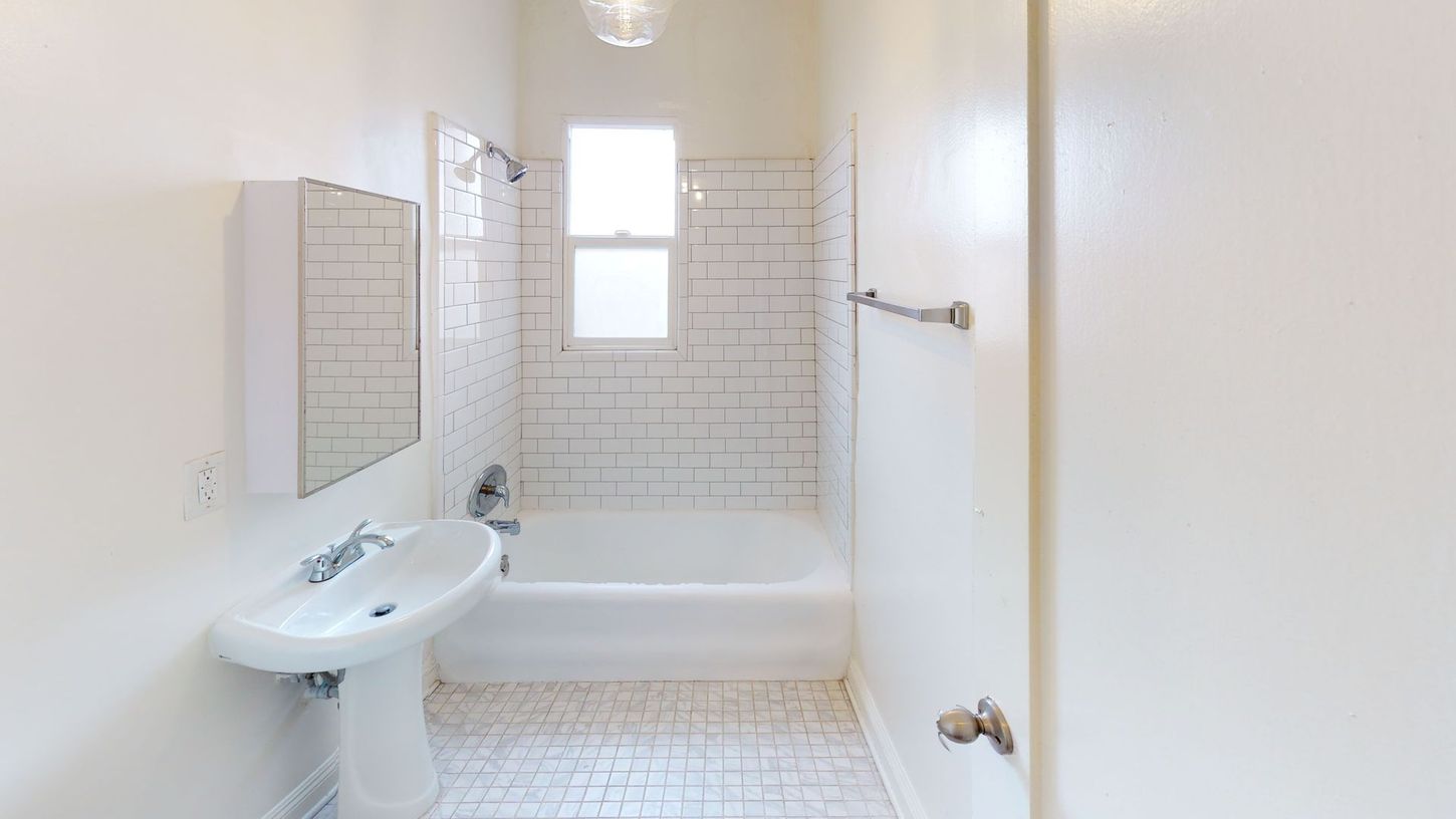 White bathroom with a tub, sink, and window.