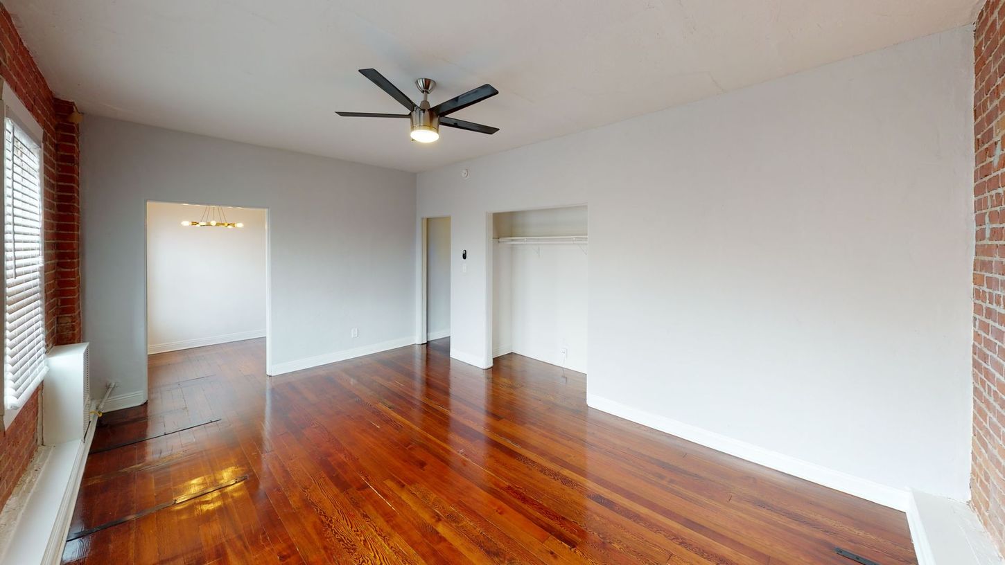 Empty room with wood floors, white walls, exposed brick, and a ceiling fan.