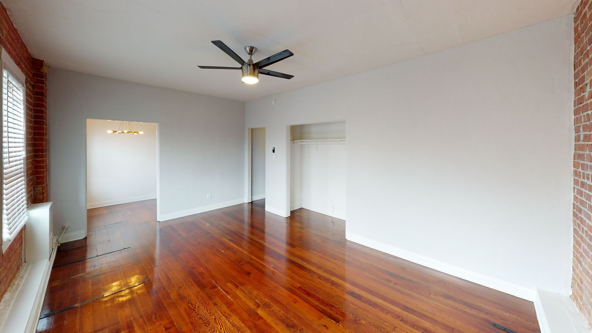Empty room with wood floors, white walls, exposed brick, and a ceiling fan.