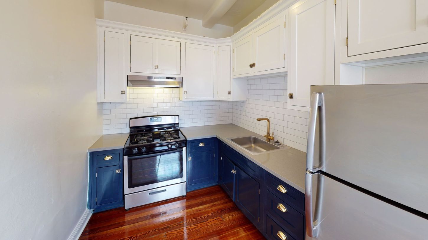 Kitchen with white and blue cabinets, stainless steel appliances, and wooden floor.
