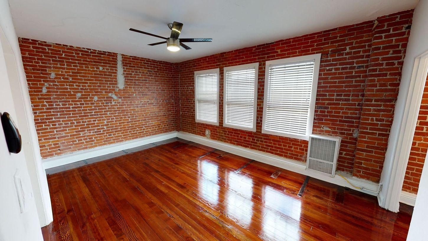 Interior room with exposed brick walls, hardwood floors, and three windows with textured coverings.