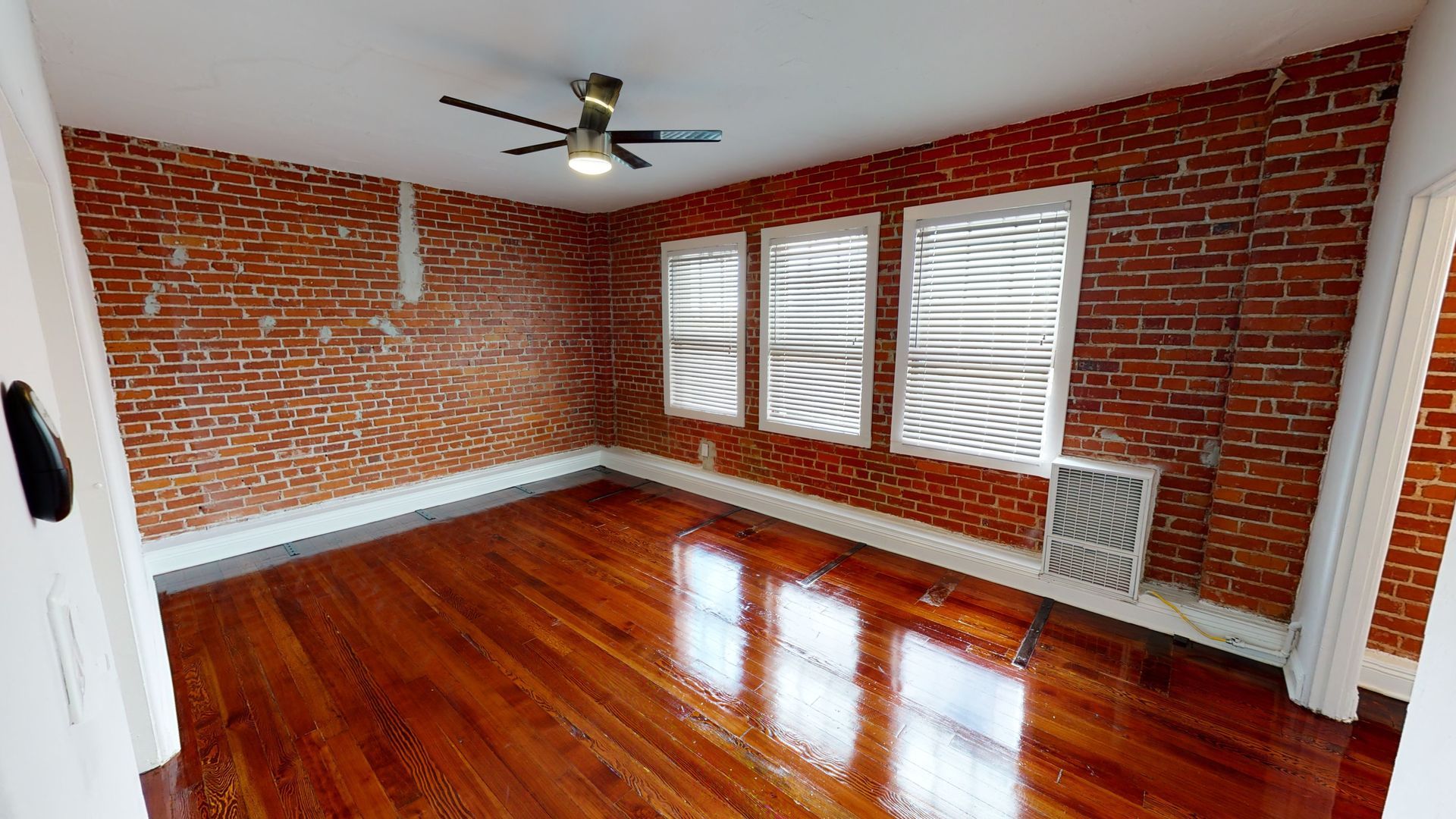 Interior room with exposed brick walls, hardwood floors, and three windows with textured coverings.