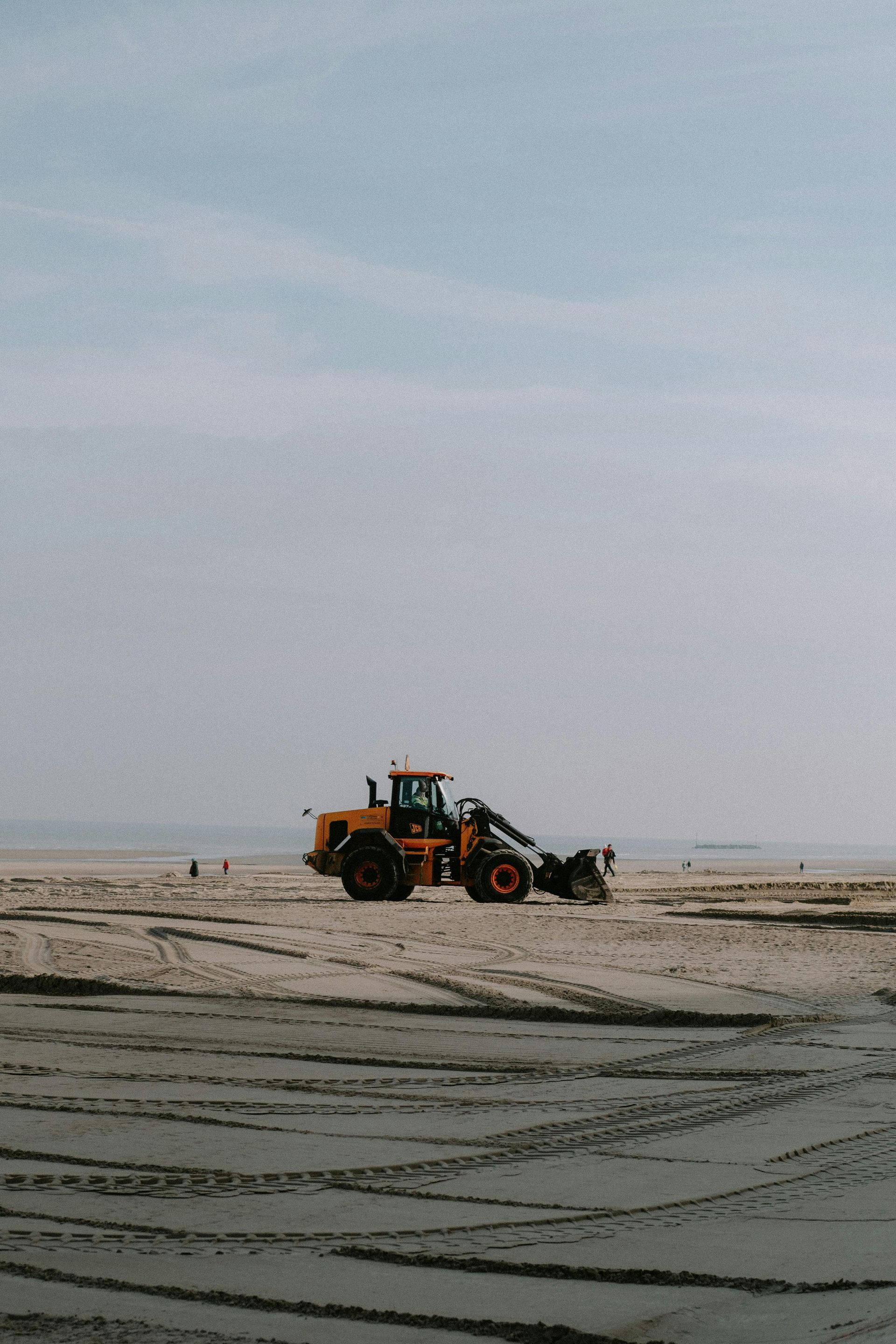 Yellow construction vehicle on a beach, working in the sand. Sky overhead.