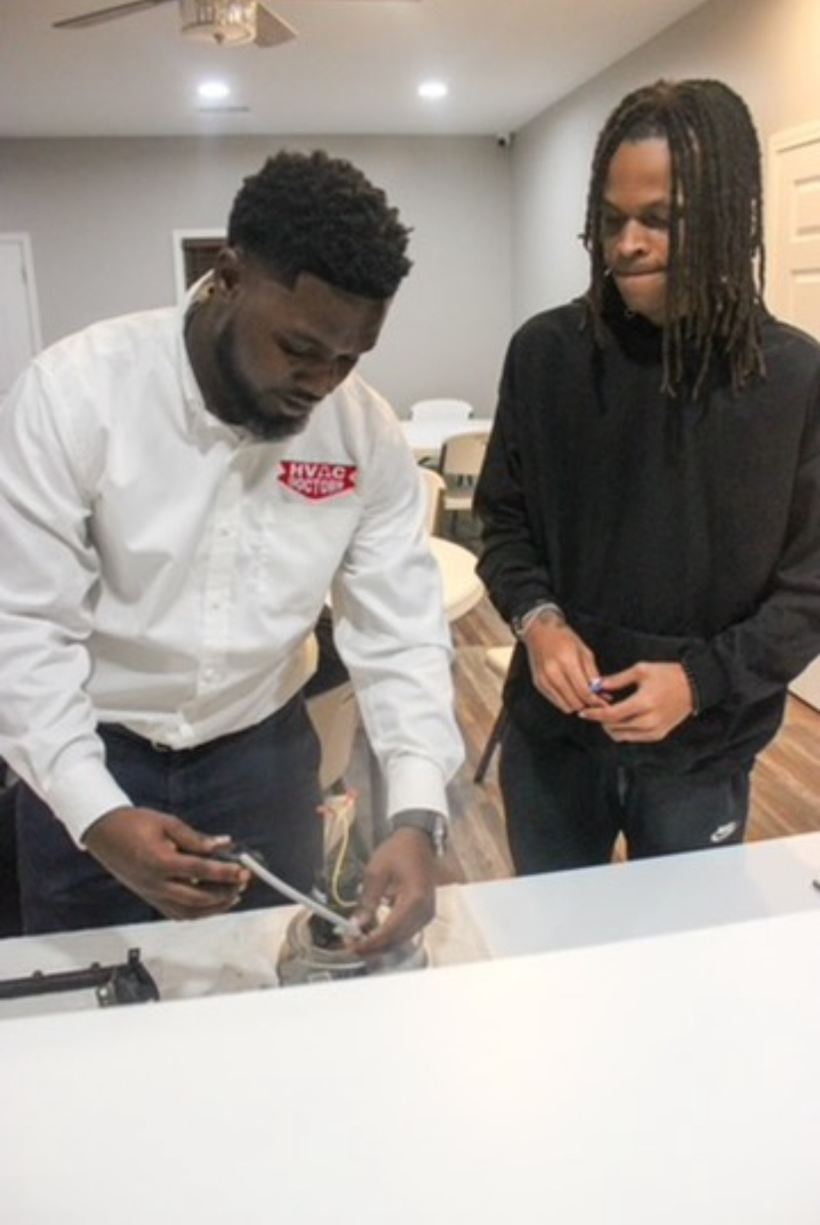 Two men are standing next to each other looking at something on a table.