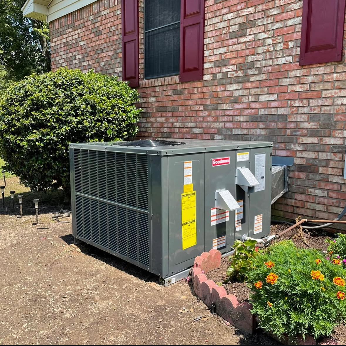 A large air conditioner is sitting on the side of a brick house.