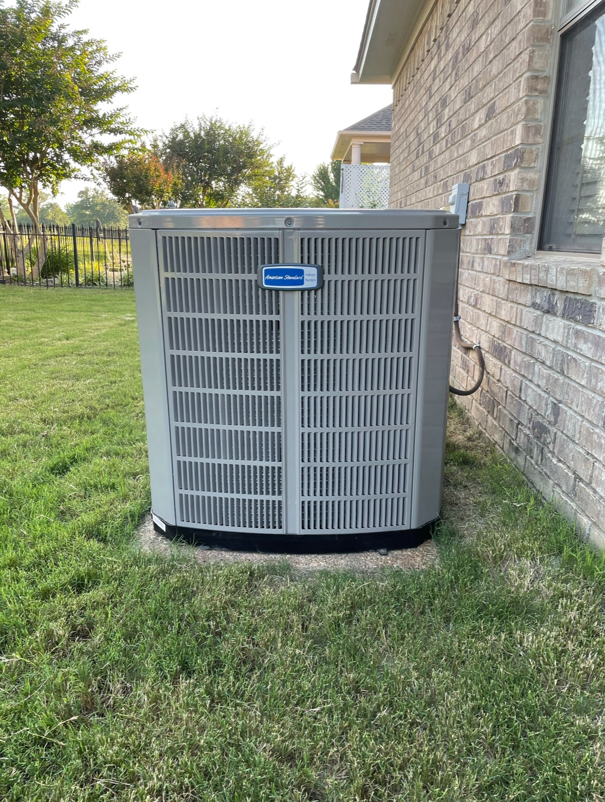 A large air conditioner is sitting in the grass next to a brick building.