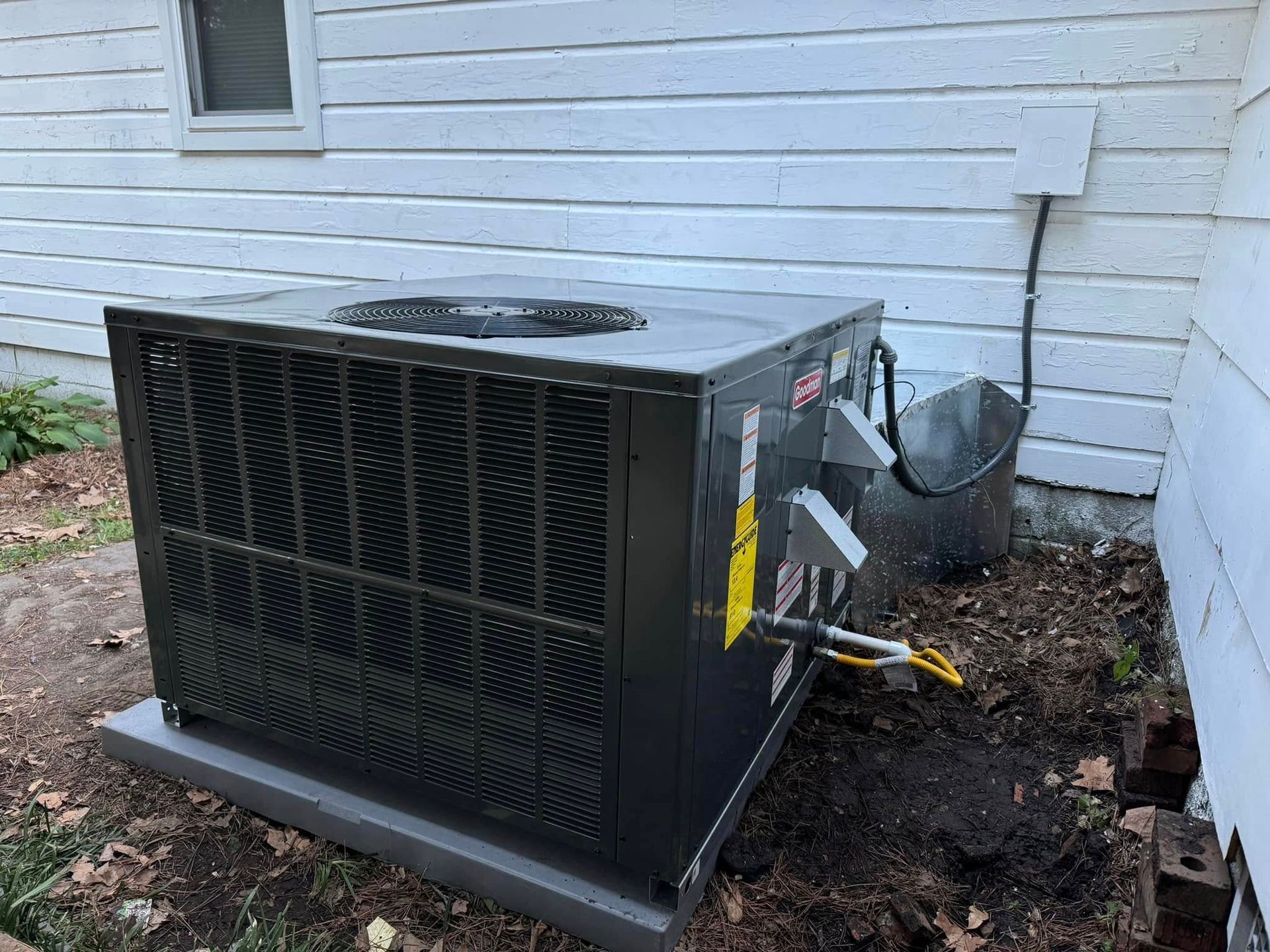 A black air conditioner is sitting on the side of a white house.