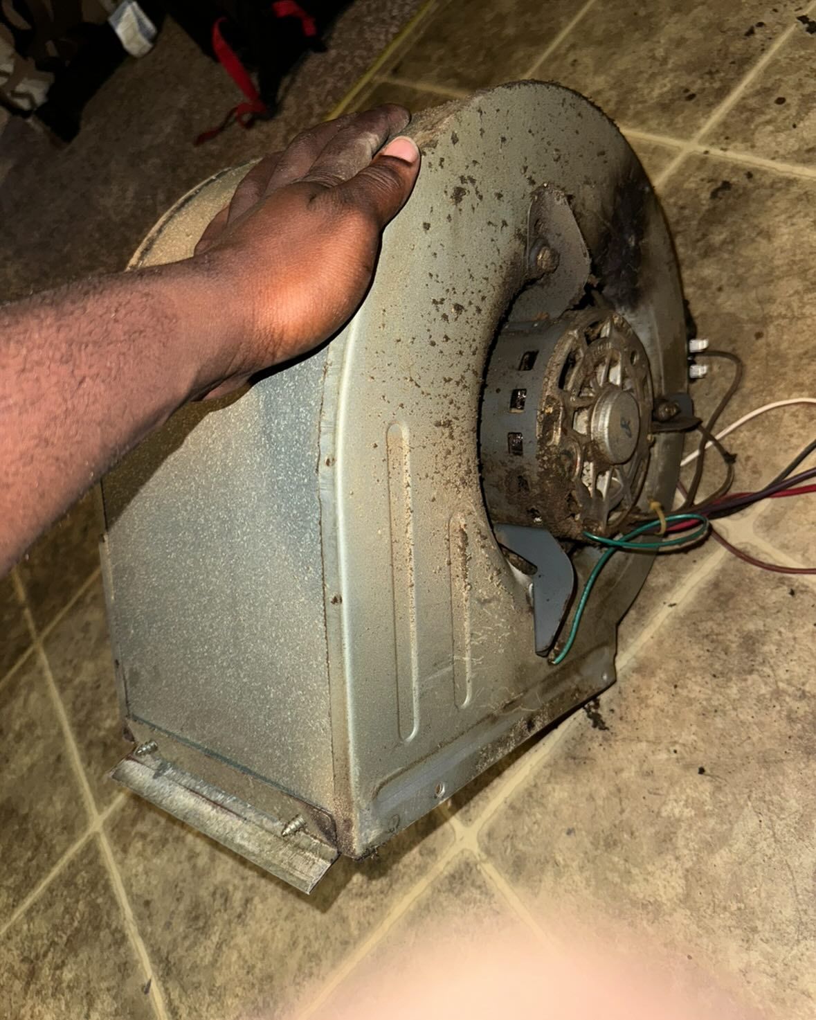A person is holding a dirty blower on a tiled floor.