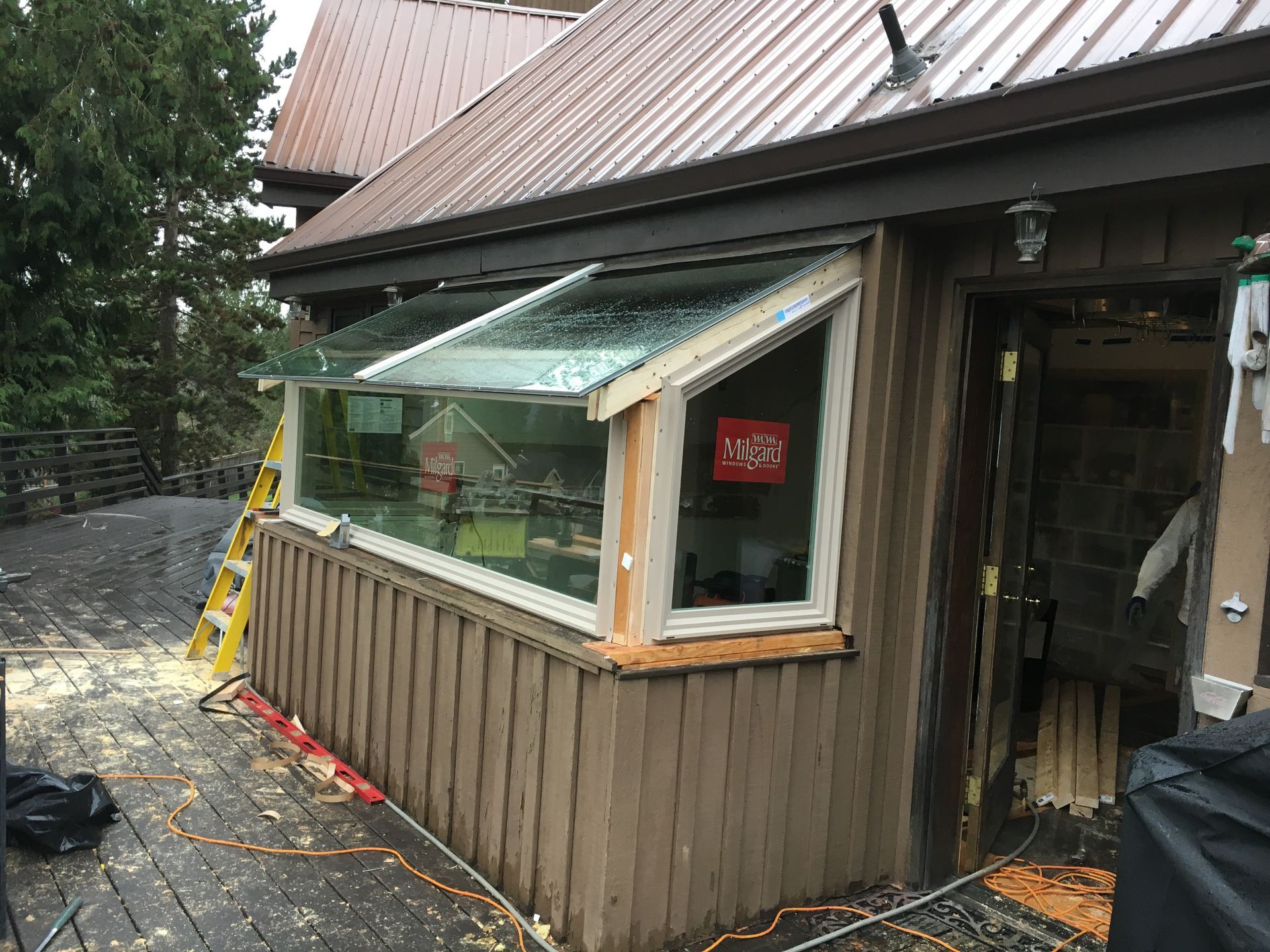 Angled window with a roof overhang on a weathered building, a ladder nearby, and debris on a wooden deck.