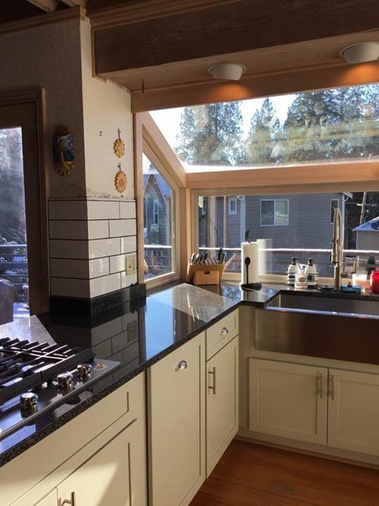 Kitchen with white cabinets, dark countertop, and large window overlooking trees.