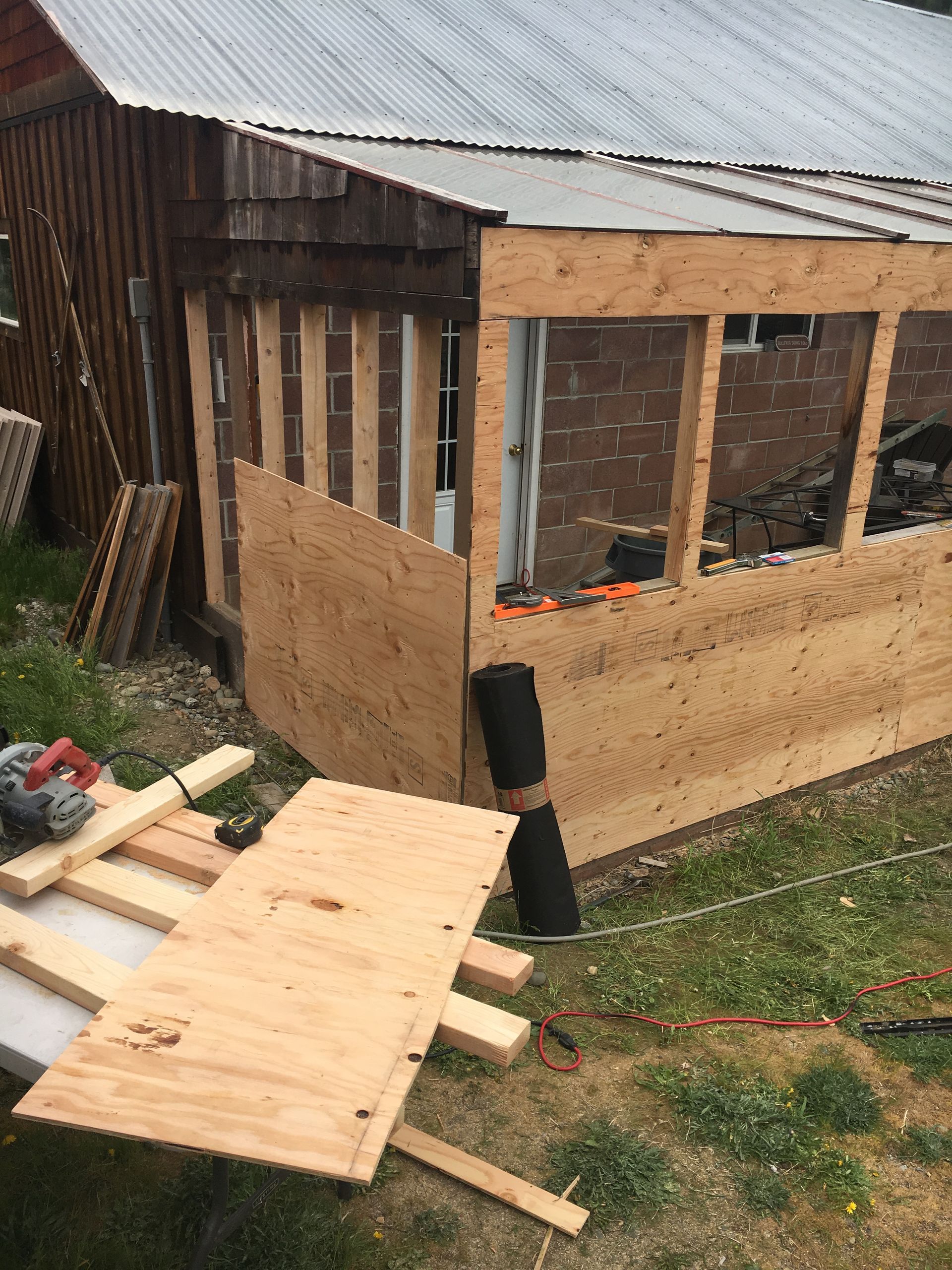 Construction site: exterior of a building with new wooden framing. Plywood and tools on the ground.