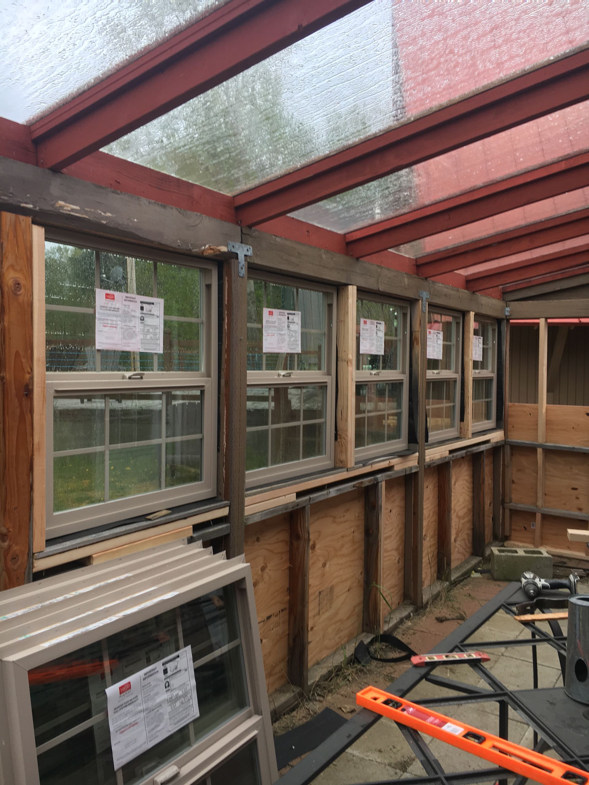 Sunroom under construction with installed windows. Brown wood frames, clear roof panels.