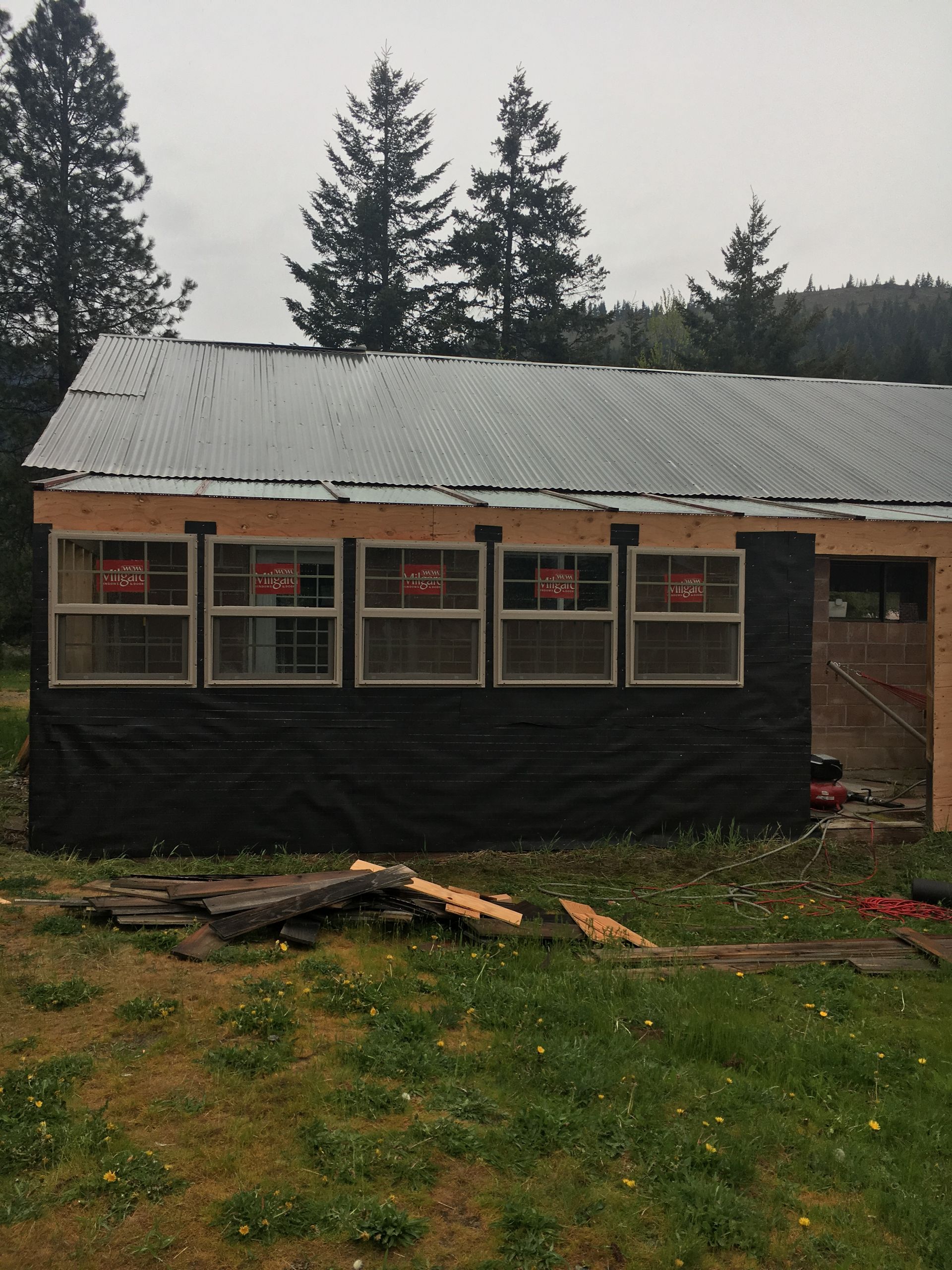 A partially built shed with five windows, black siding, and a metal roof, set in a grassy outdoor area.
