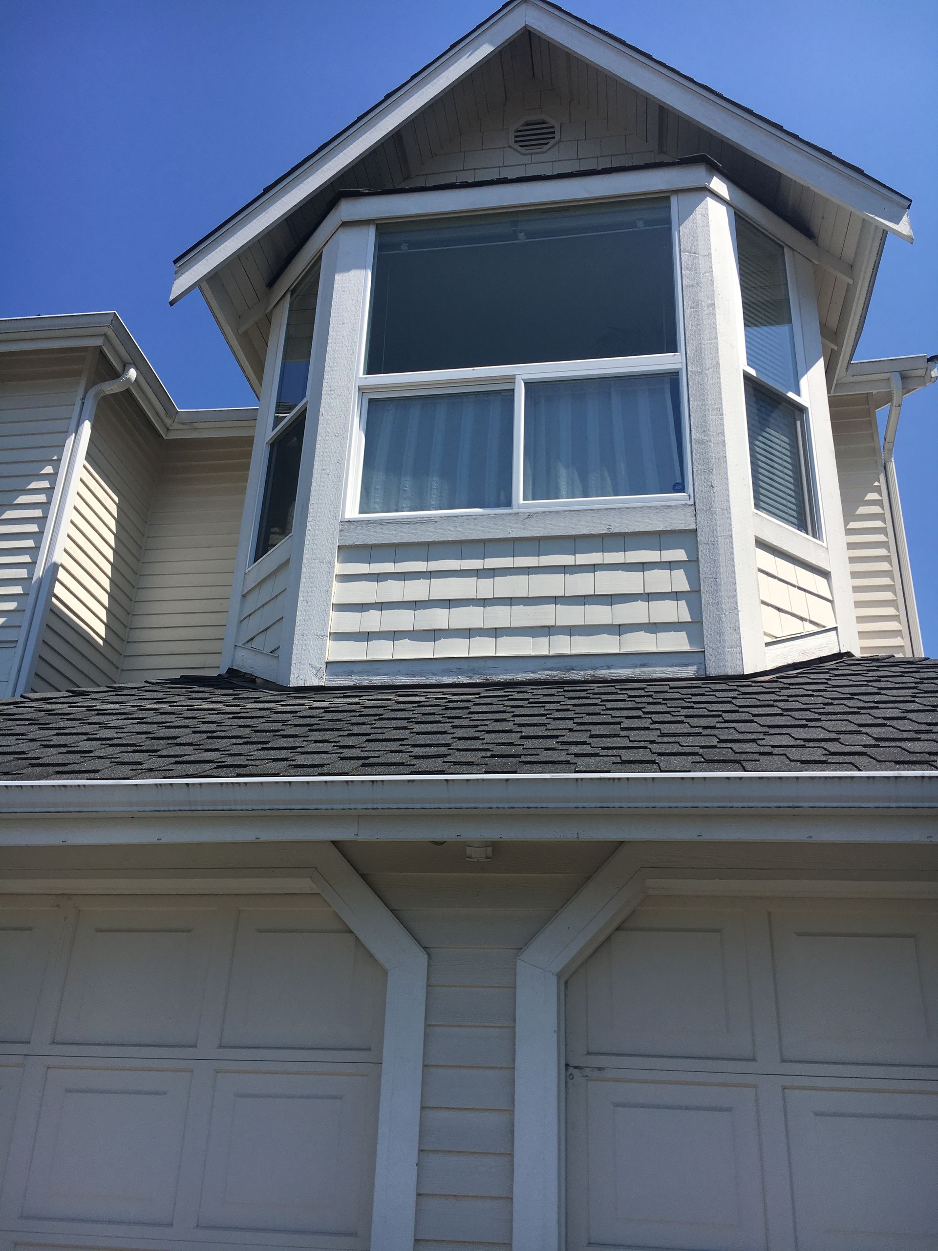 View of a house with a bay window, garage, and blue sky. Beige and white paint.