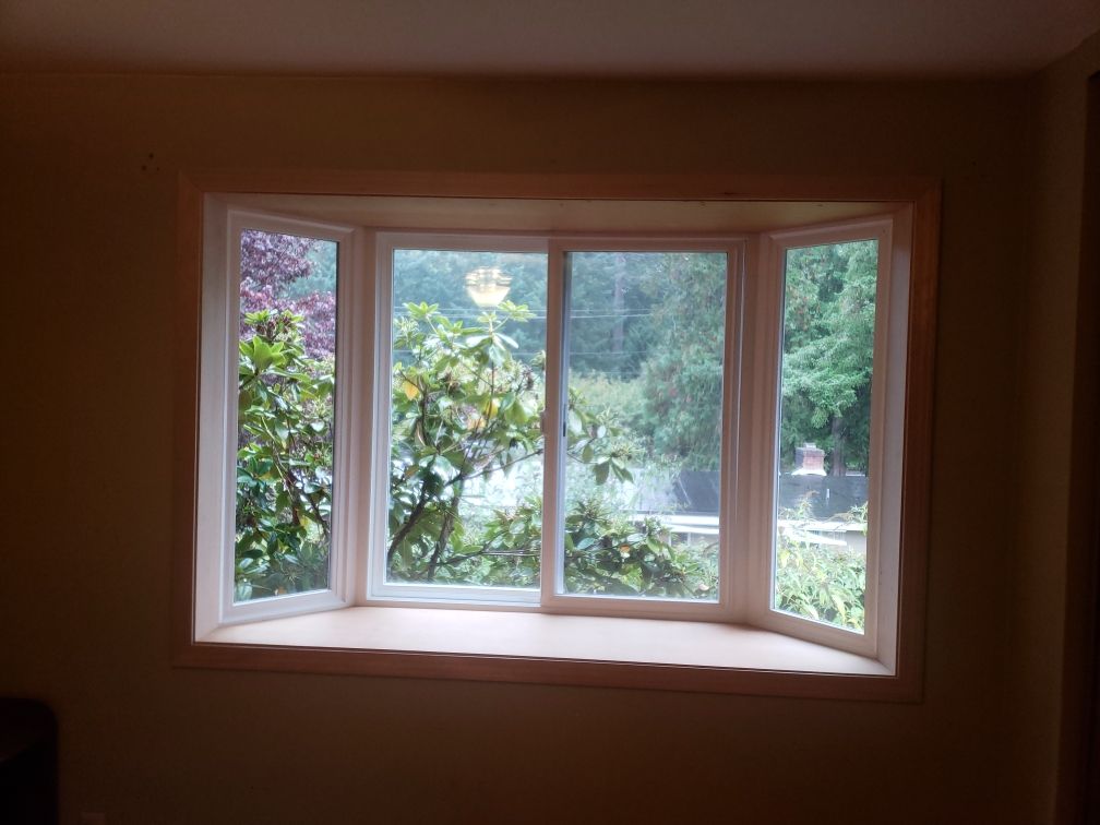 Bay window with white frame, overlooking green trees, set in a tan-walled room.