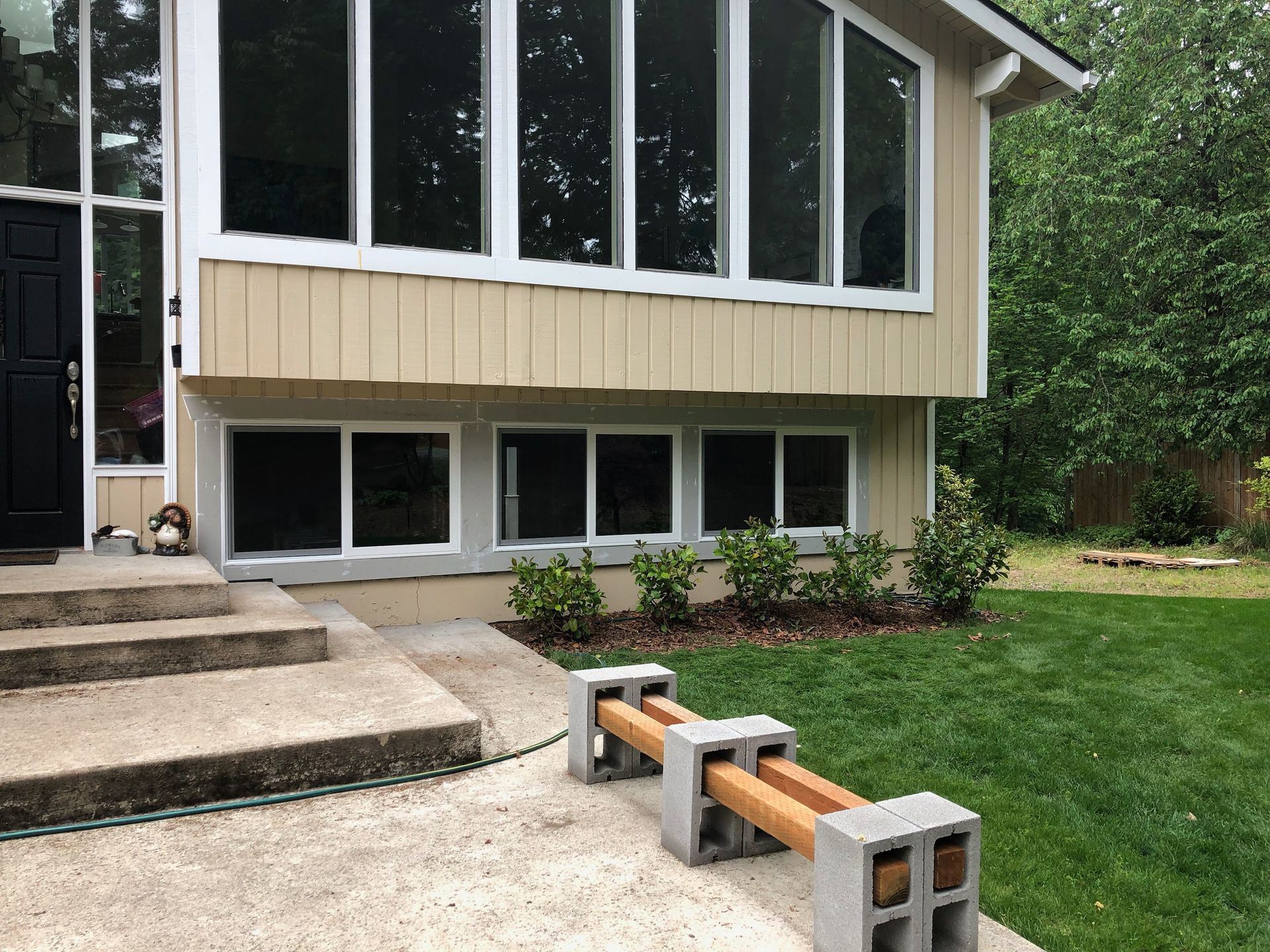 Tan house with large windows, concrete steps, and a DIY bench made of cinder blocks and wood.