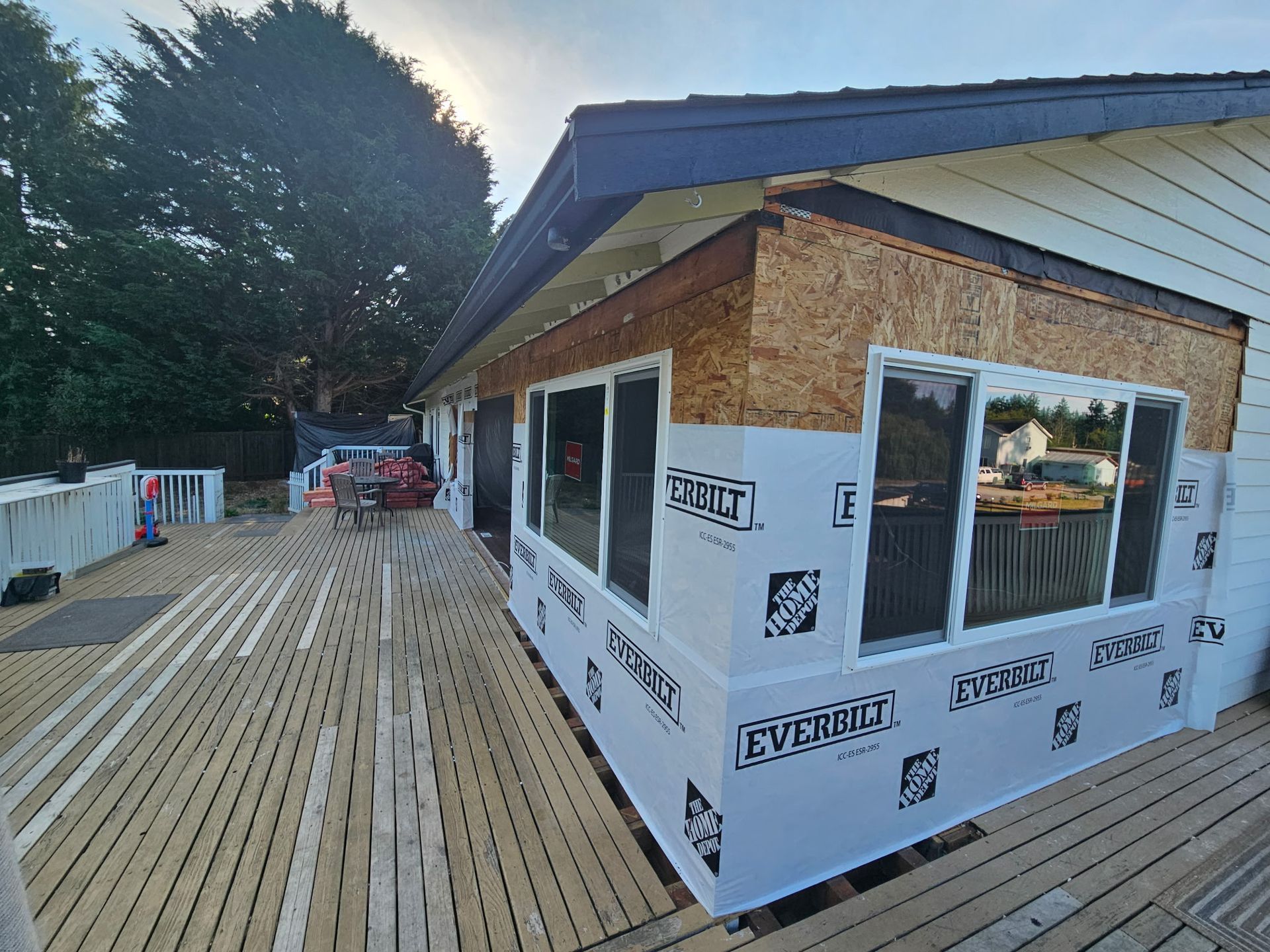 Exterior view of a house under renovation with a partially constructed deck and exposed framing and siding.