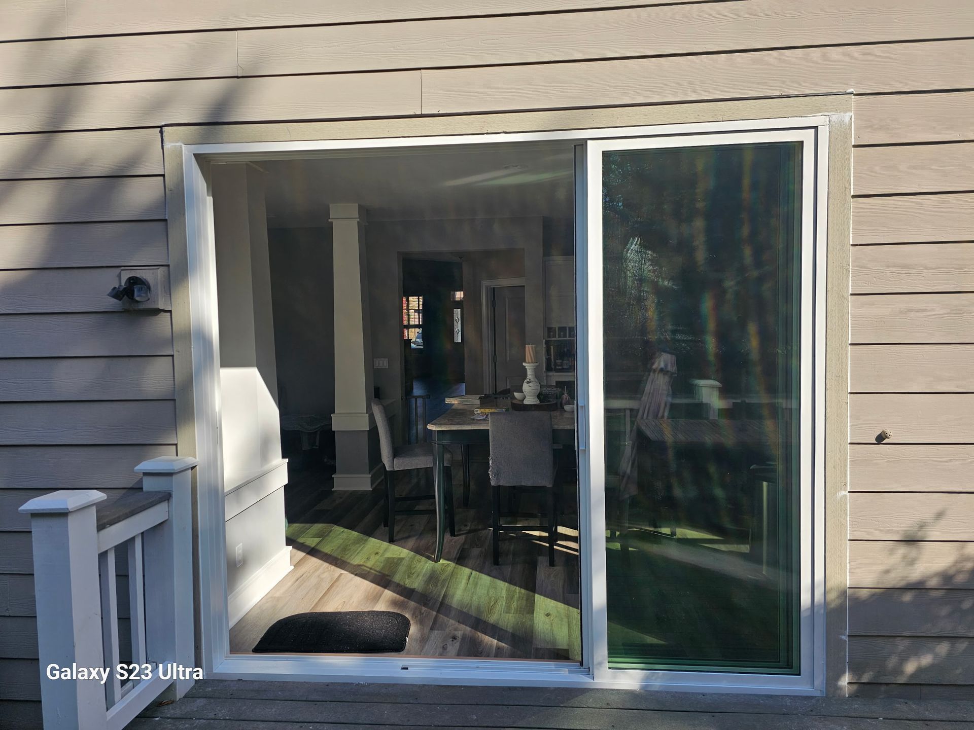 Sliding glass door on a house, showing interior with dining table and chairs; bright sunlight.