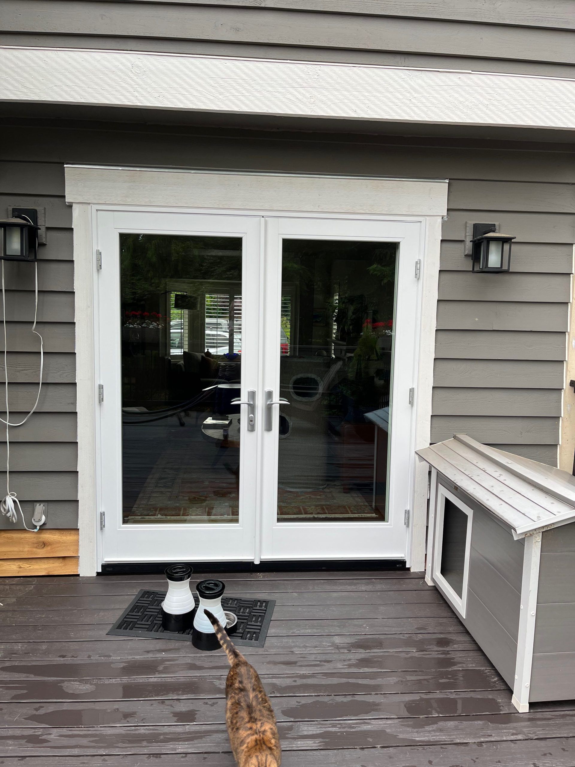 White double glass doors on a grey house, with a cat, pet house, and outdoor lights.