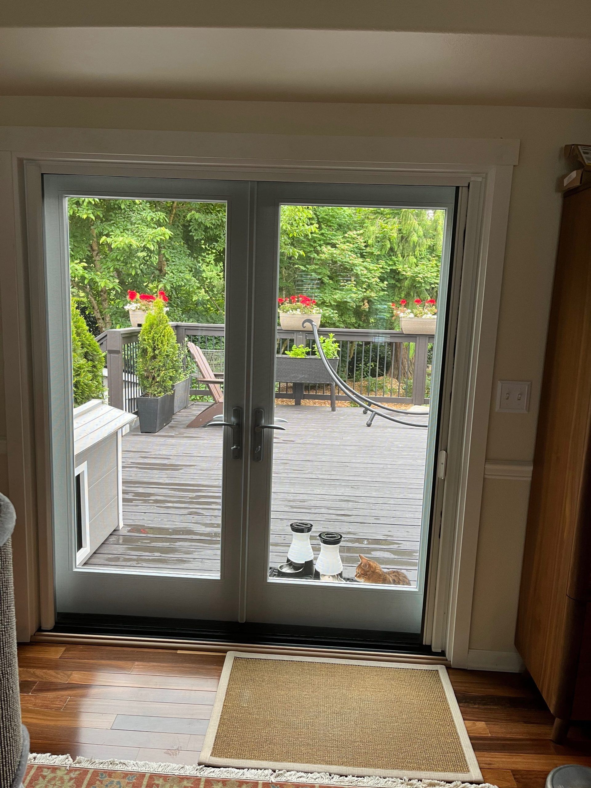 Glass doors open to a wooden deck with greenery, potted plants, and seating.