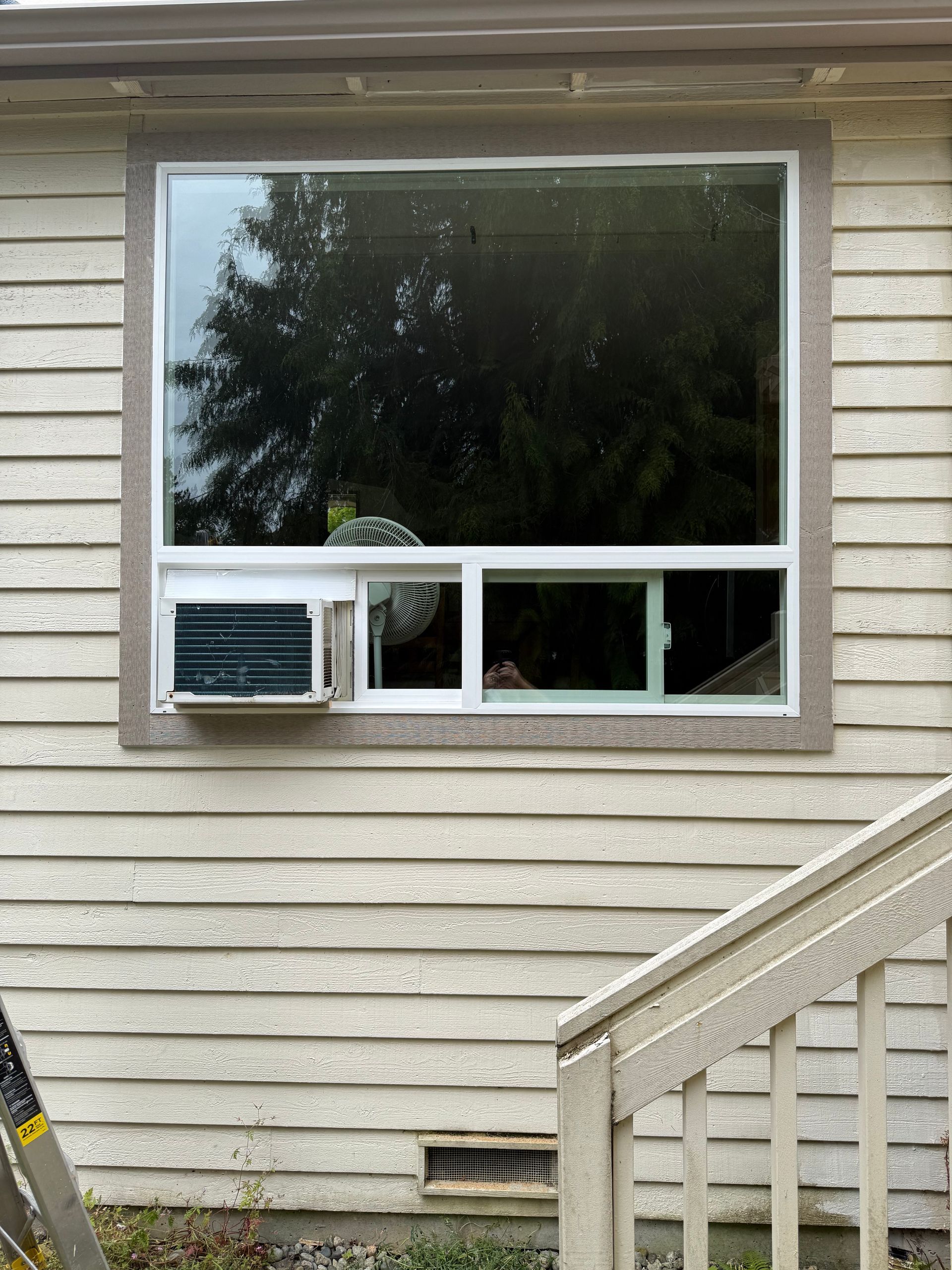 Window with air conditioner, white frame, and gray siding. Exterior view with a staircase visible on the right.