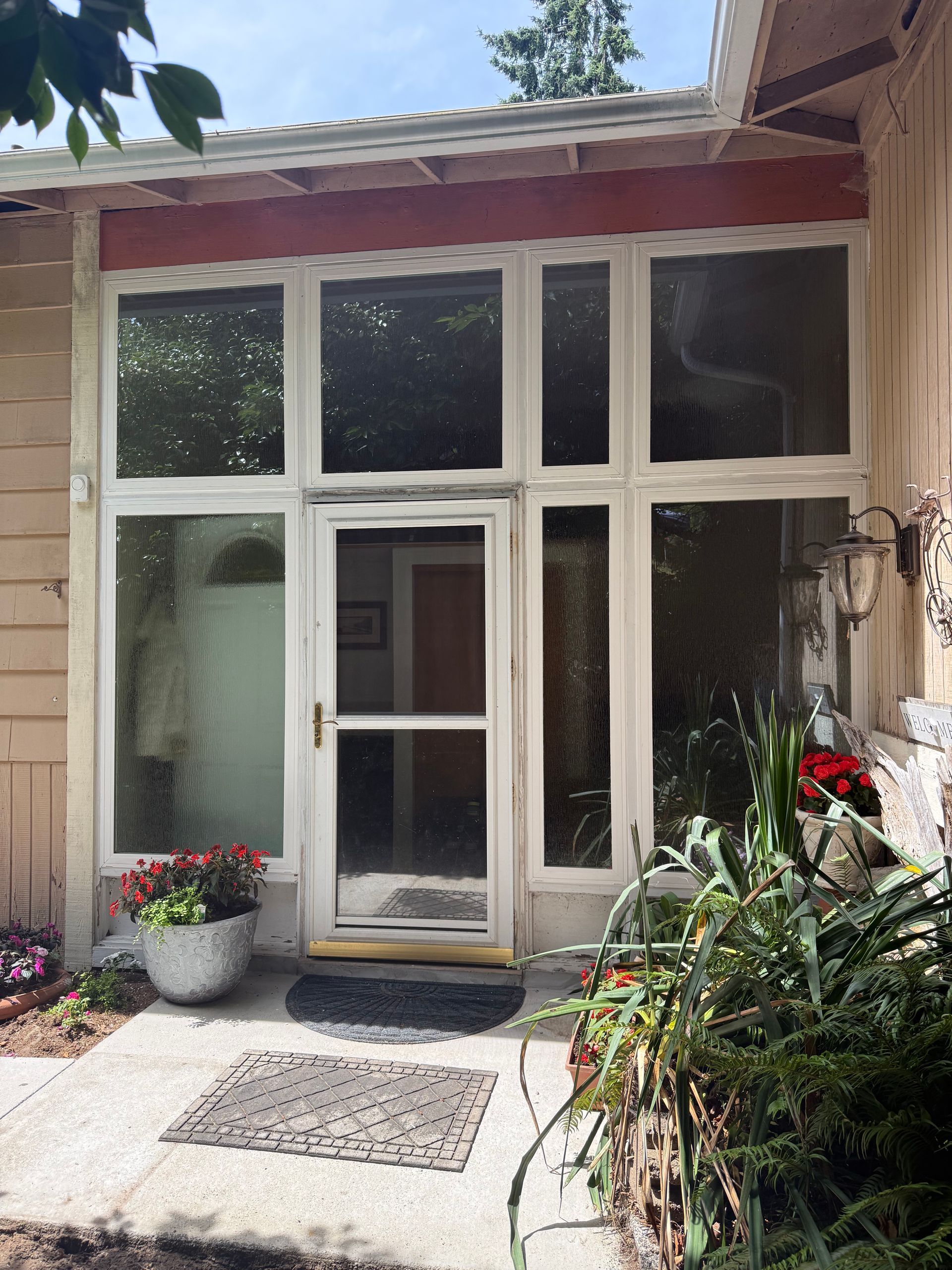 Entryway with white-framed windows, a screen door, and potted plants in a residential setting.