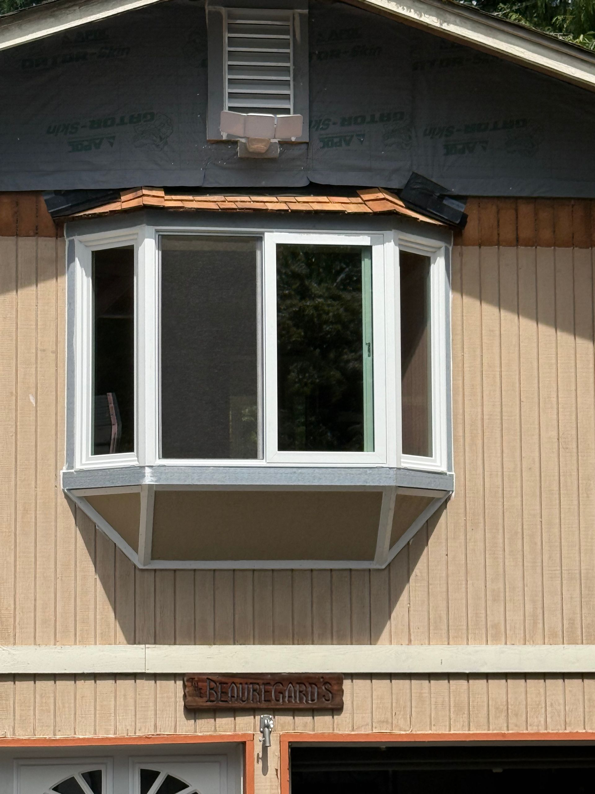 Bay window on a tan building, with a small attic vent above.
