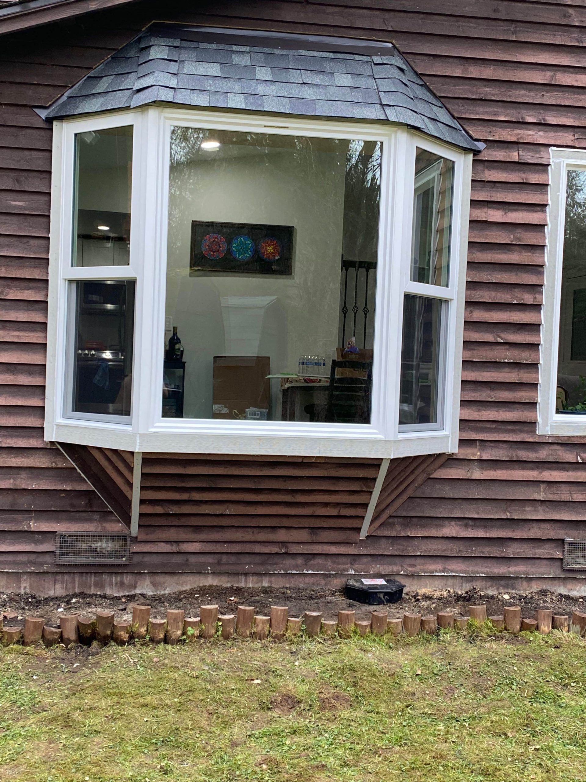 Bay window on a brown wooden house; view of a room with desk and art.
