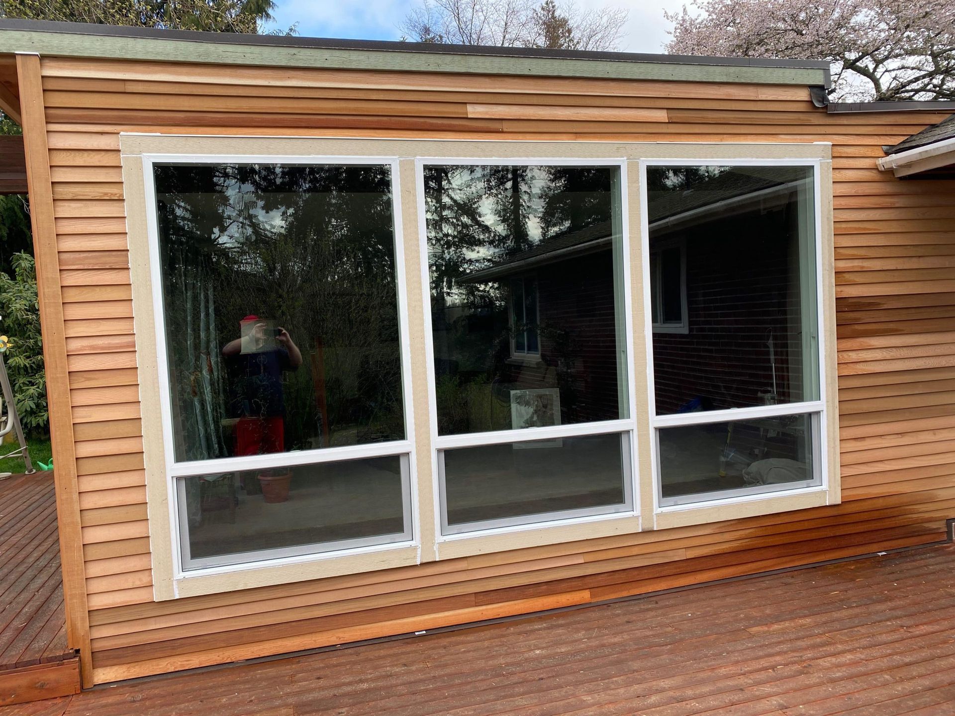 Three large windows in a wood-sided structure with a wooden deck.