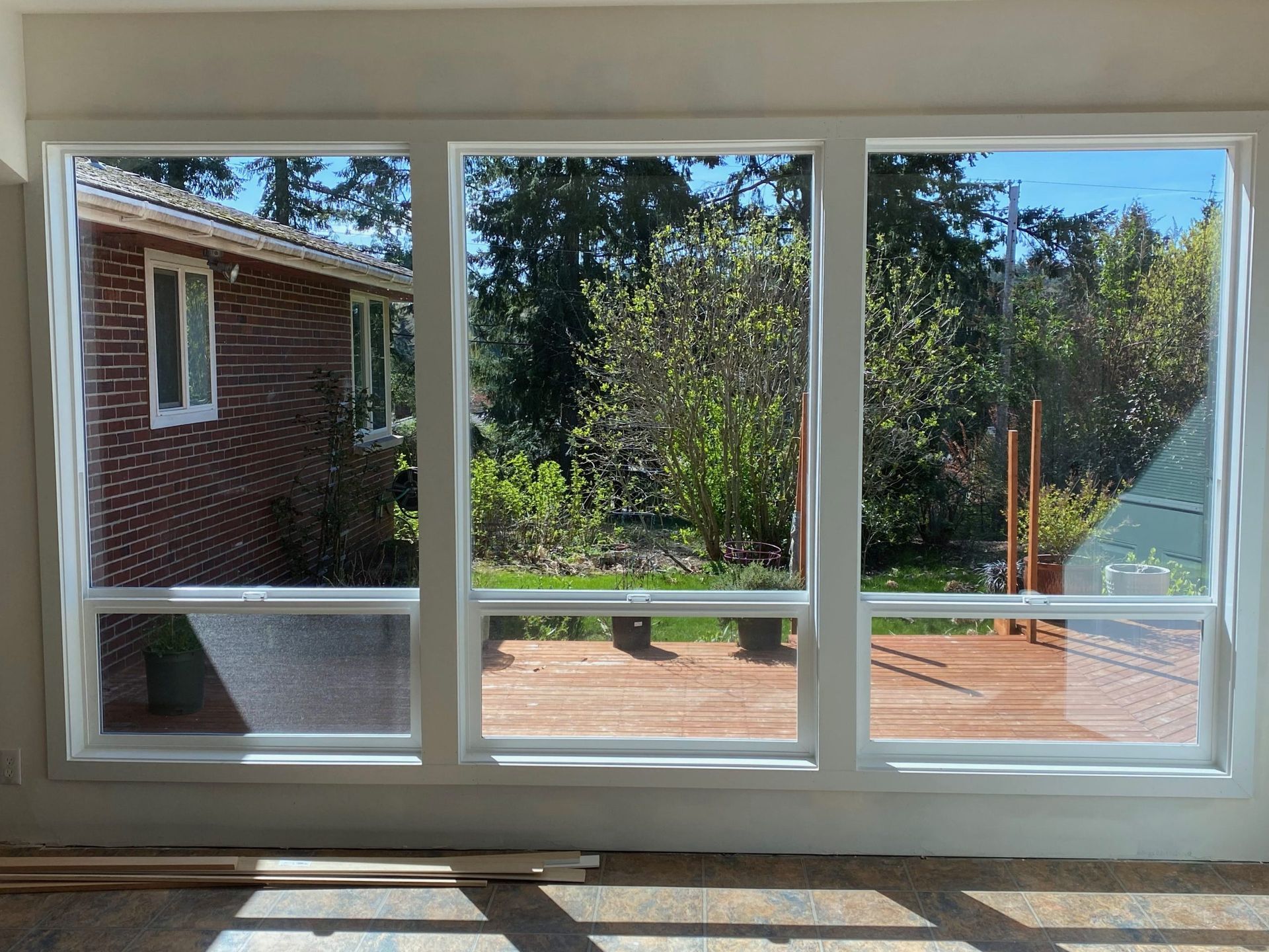 Three-panel window view of a red brick house, a wooden deck, and green trees in the background on a sunny day.