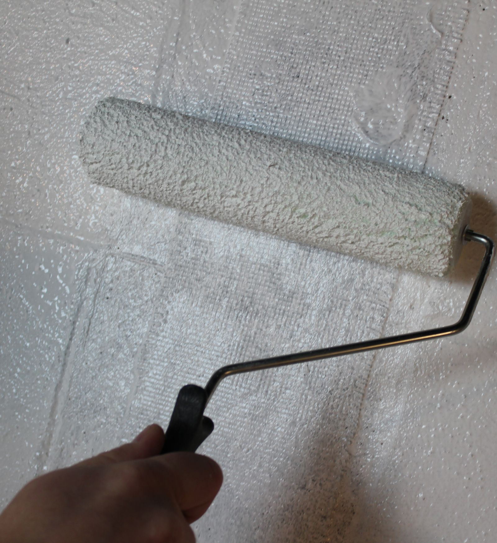 a person is painting a white wall with a paint roller sealing a basement wall