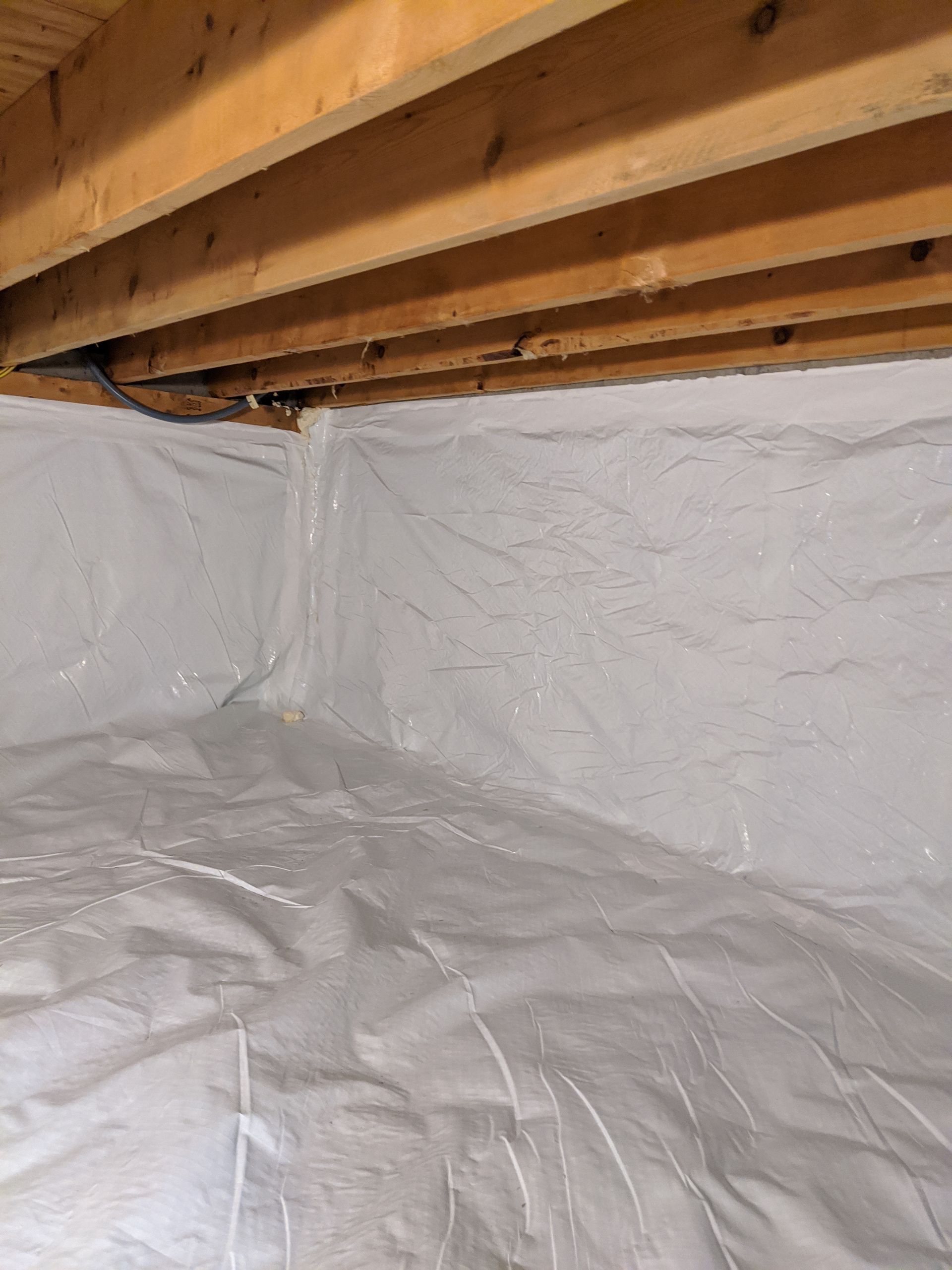 a basement crawlspace covered in plastic and wooden beams 