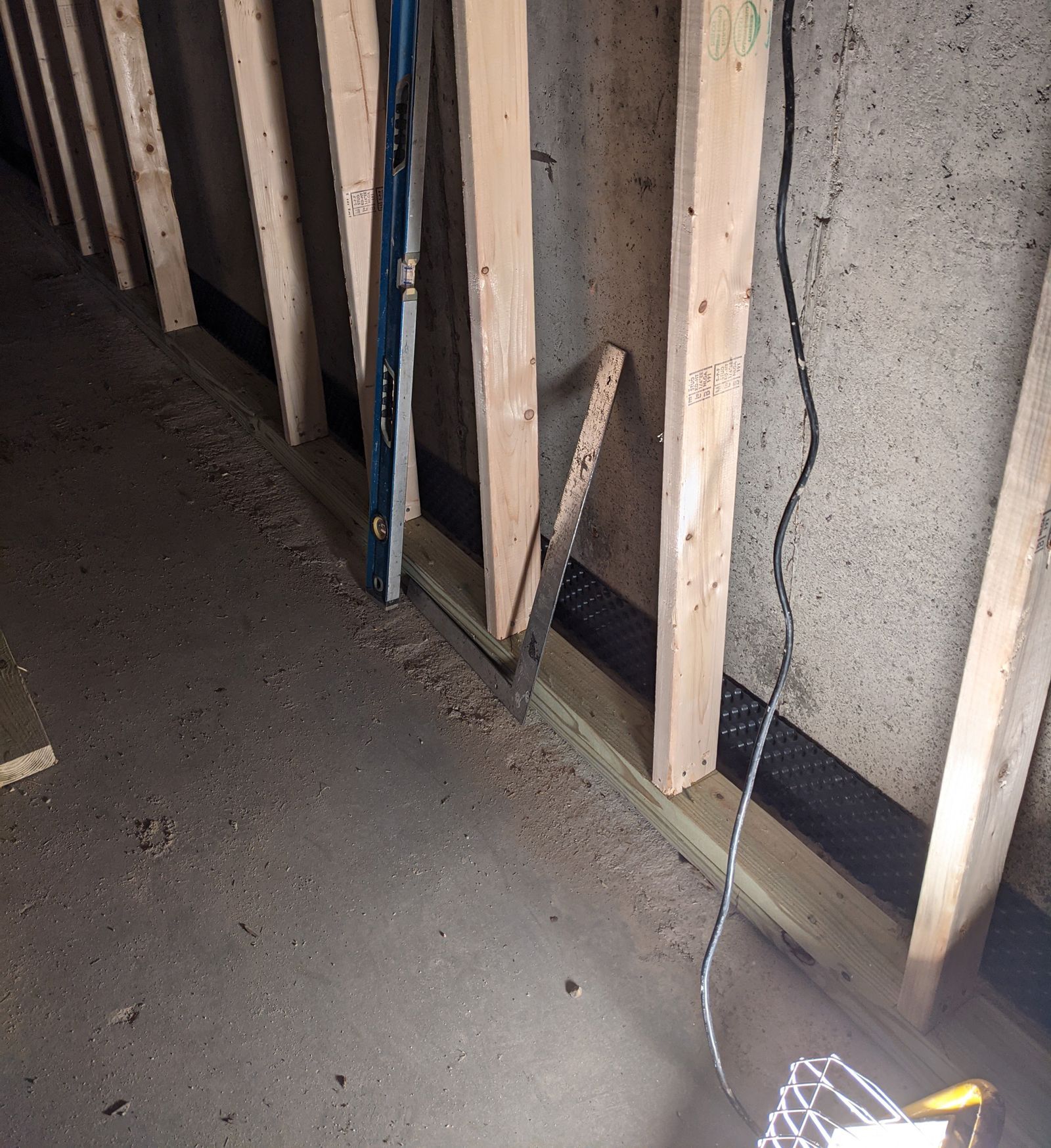 basement waterproofing project showing a wooden wall with a ladder and a light on the floor 