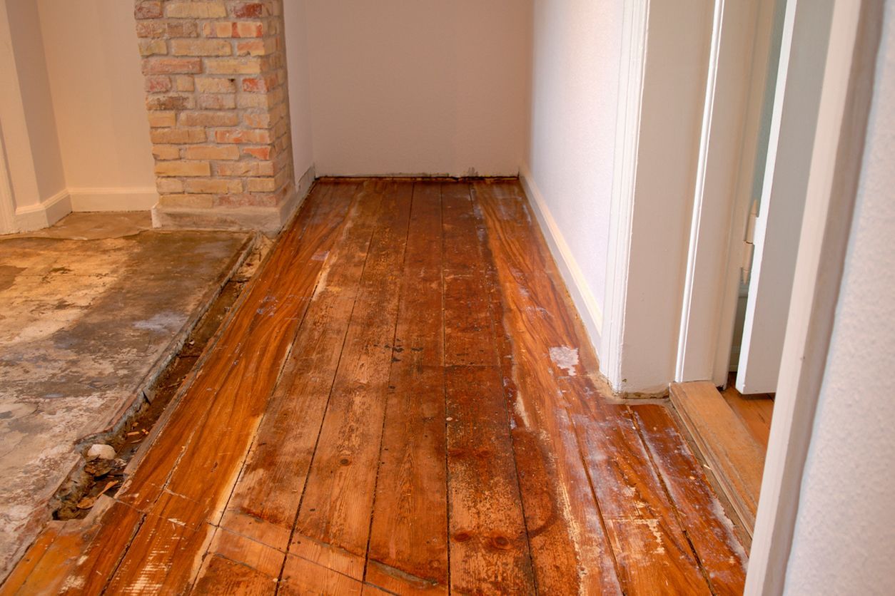 a hallway with a wooden floor and a brick wall showing water damage