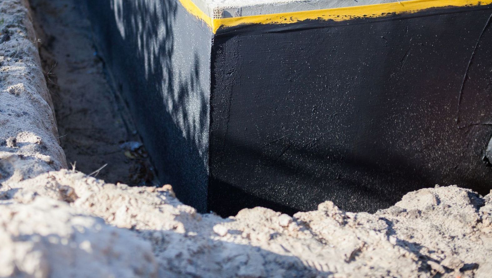 A person is digging a hole in the ground next to a wall.