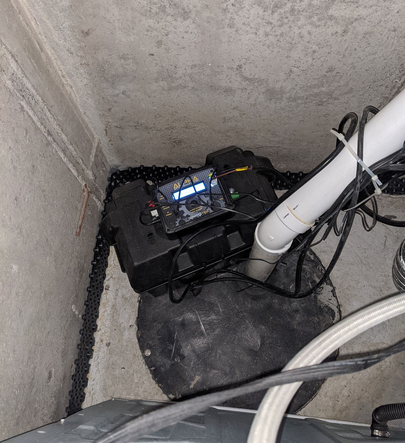 sump pump for a home is sitting on the basement floor next to a white pipe .