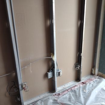 Interior wall under construction, with metal studs, exposed wiring, and electrical boxes.