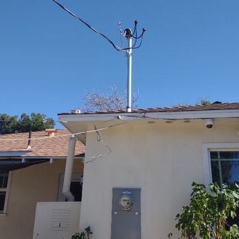 Utility pole atop a house with power lines against a blue sky.  A meter box is visible on the wall.
