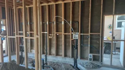 Framed interior wall under construction with plumbing and electrical work exposed.