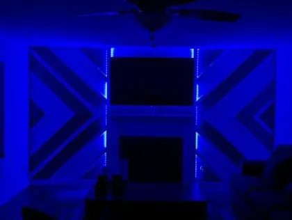 Blue LED lights illuminate a geometric wall design with a TV and fireplace. Dark room with furniture silhouettes.