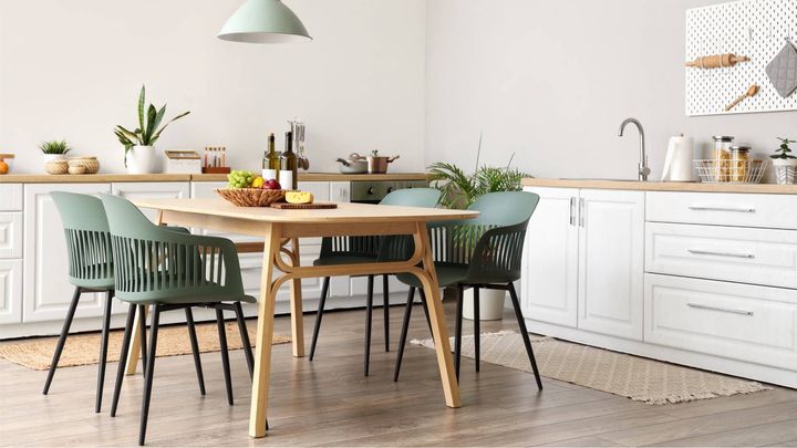 Kitchen with a wooden table, four green chairs, white cabinets, and plants.