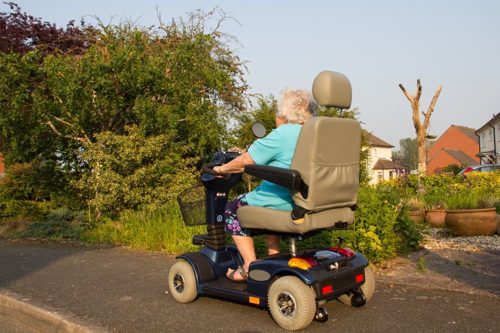 An Elderly Woman Is Riding a Mobility Scooter Down a Street — VAL Disability Services in Taree, NSW