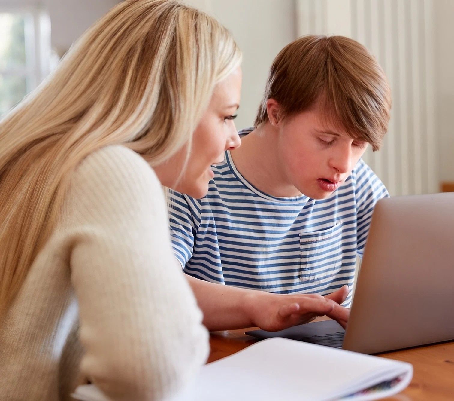 Two people play acoustic guitars at a table indoors. One is older, the other younger. Sunlight streams in the windows. — VAL Disability Services in Taree, NSW
