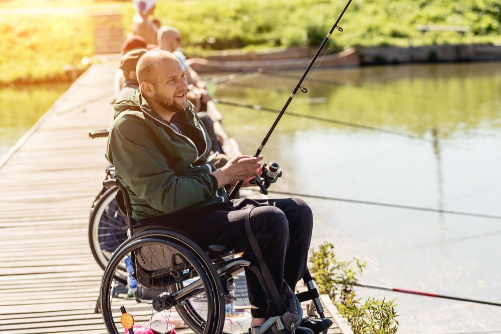A Man in A Wheelchair Is Fishing on A Pier — VAL Disability Services in Taree, NSW